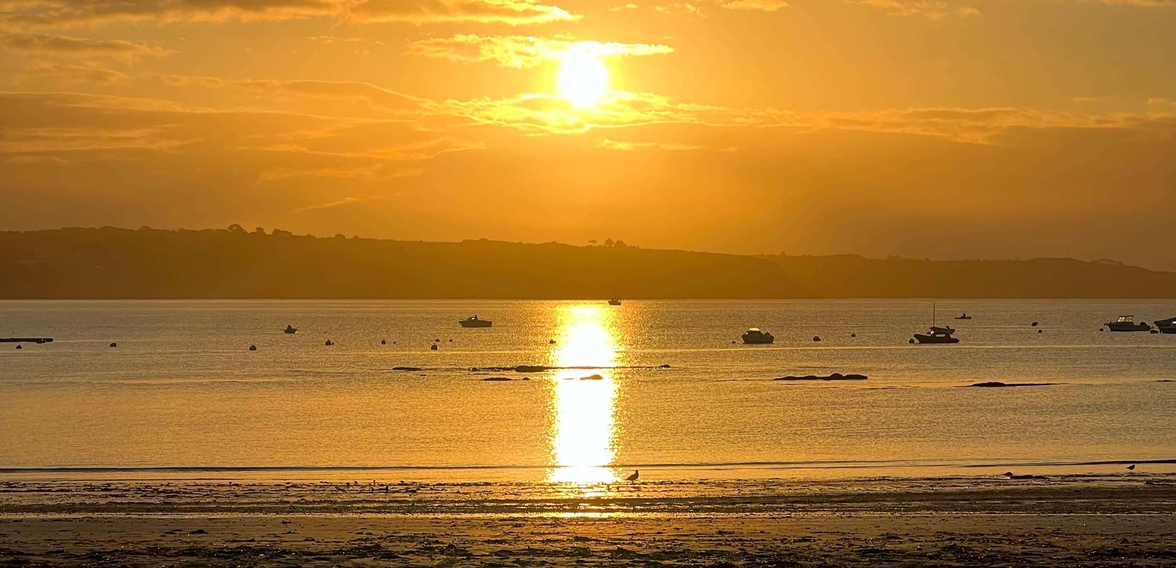 La plage du Trez-Hir à Plougonvelin au coucher du soleil, bateaux au mouillage et reflet doré sur la mer.